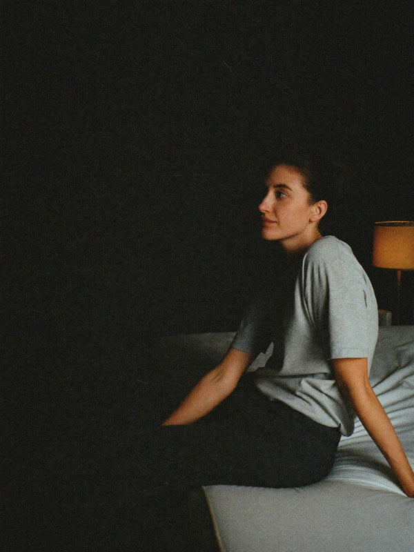 Woman winding down on the edge of her bed in a dark bedroom at night