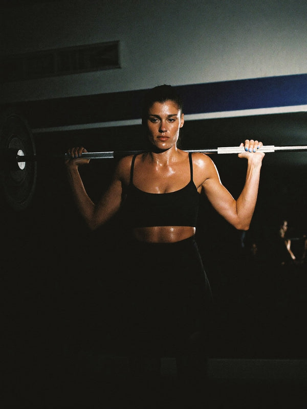 Woman in her thirties lifting a barbell in a dimly lit gym