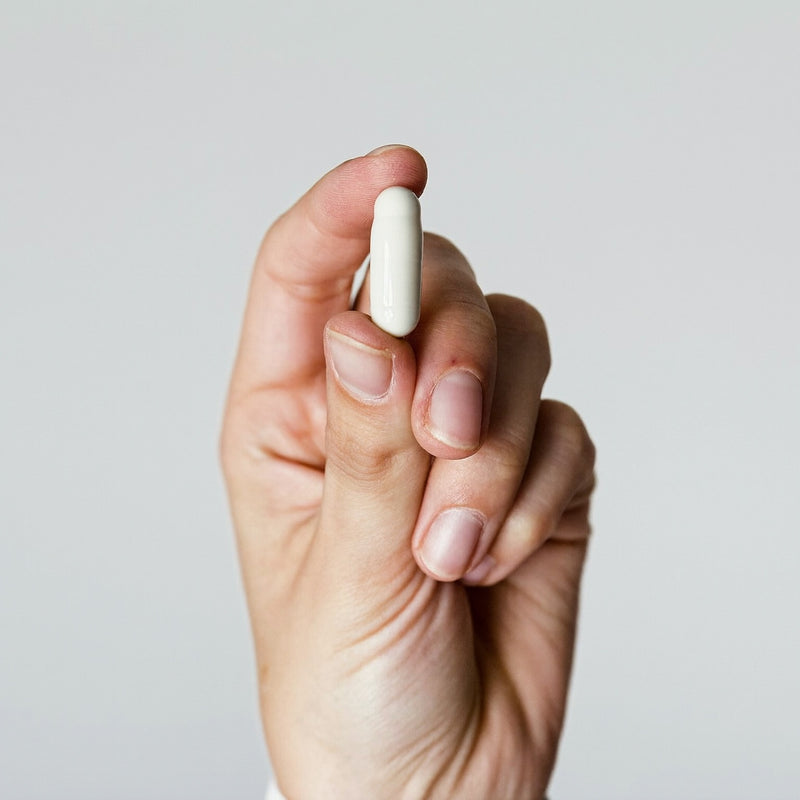 Hand holding a single plain white supplement capsule